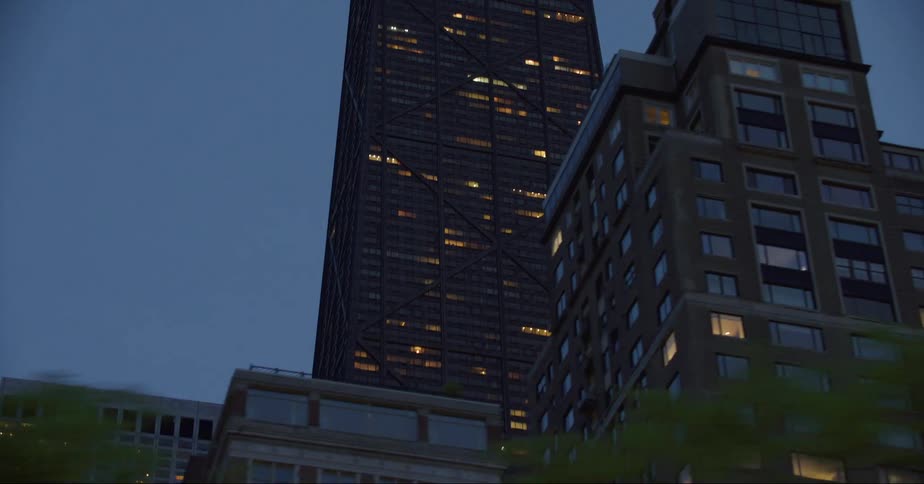 Illuminated skyscraper with spires and apartment buildings against the sky at dusk