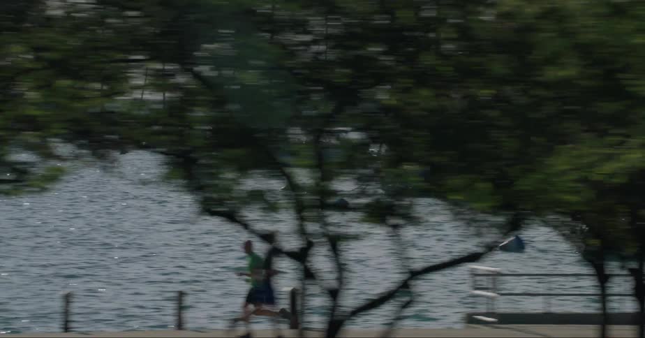 People sail boats and jog along the lake front next to a highway