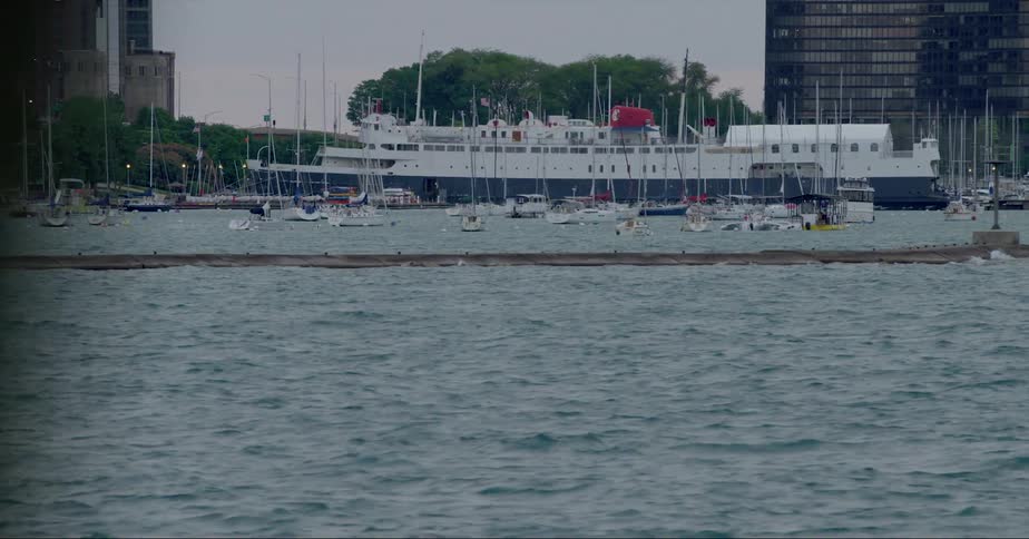 Harbor on the coast with sailboats and ferry boat with high rise buildings in the background