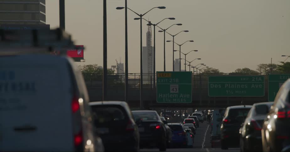 Traffic moves along highway during rush hour with digital bulletin boards and skyscrapers in the background