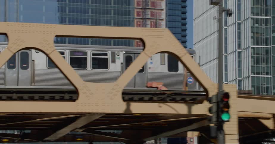 Metro train driving on the chicago elevated track over the city street under a bright blue sky
