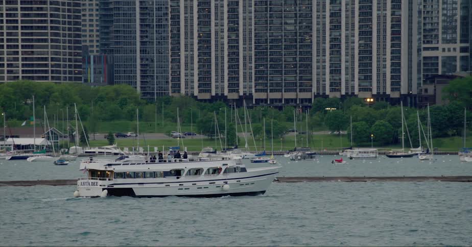 People sailing on a boat on a river with cars driving and apartment buildings in the background