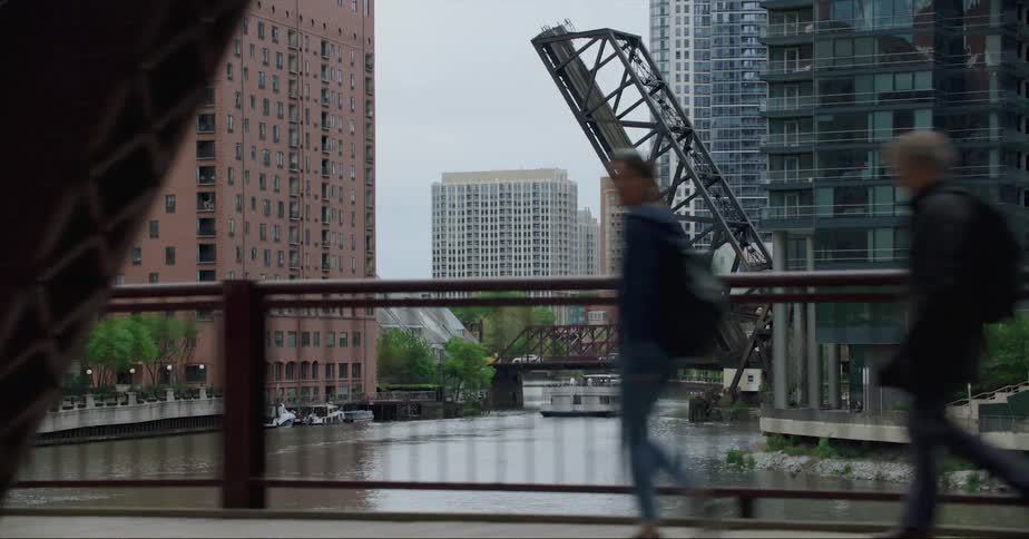 Pedestrians and traffic cross bridge as boats move under drawbridge near apartment buildings