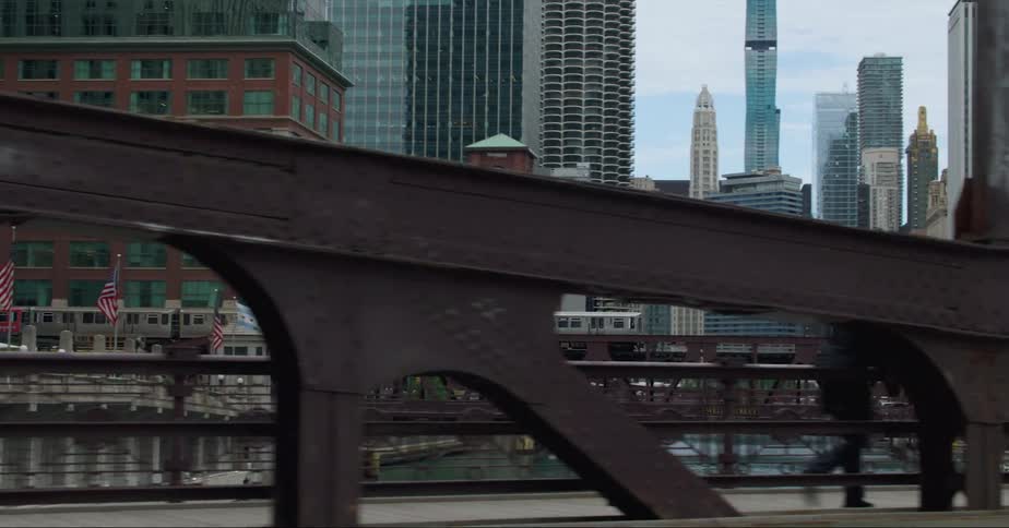 Passenger train crosses bridge over river between high rise buildings in the city