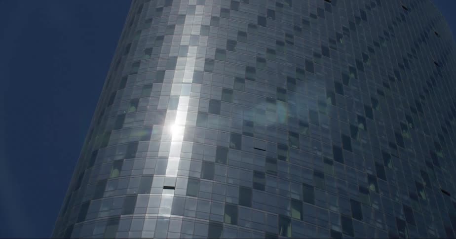 The curved facade of a skyscraper reflects sunlight against a blue sky