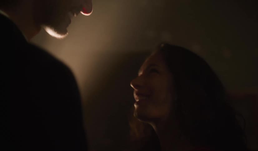 Woman with straight hair looking at man wearing black sweater laughing and talking in dark room