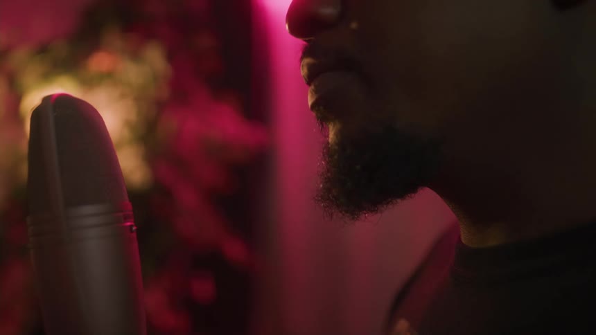 Close up of the mouth of a bearded young man singing into a microphone on a room with red lights
