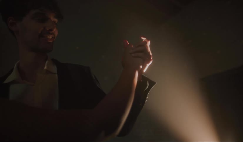 A young man and woman swaying as they slow dance with lights and shadow playing on the wall