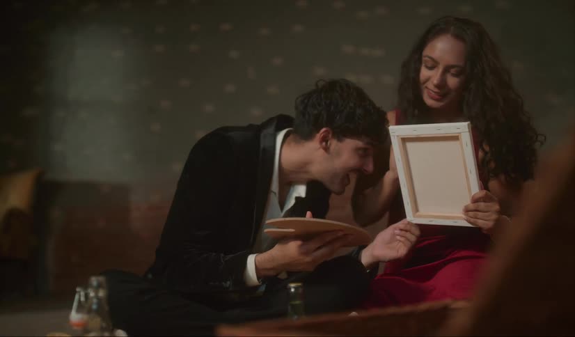 Young happy couple casually and playfully painting on canvas with oil on a party