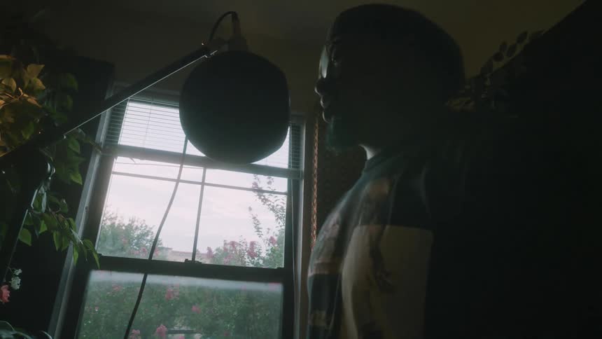 A man at home dances as he sings in to a microphone while he records himself