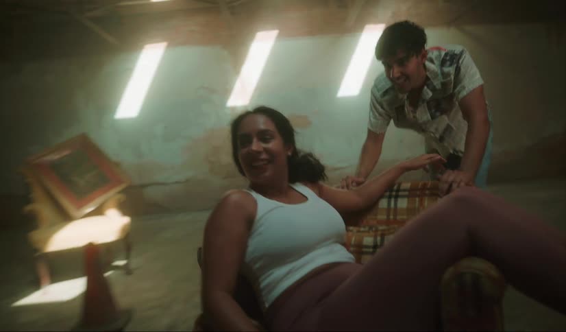 A man and woman laugh as he pushes her across a room in a chair