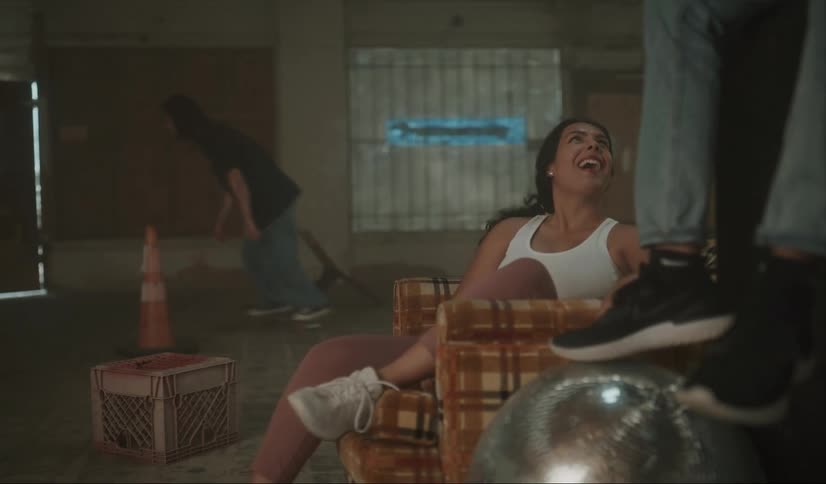 A woman talking to a man laughs as their friend skateboards over a crate in a house