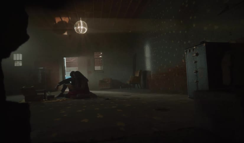 Silhouette of a young couple sitting on the floor of an abandoned warehouse under a mirror ball