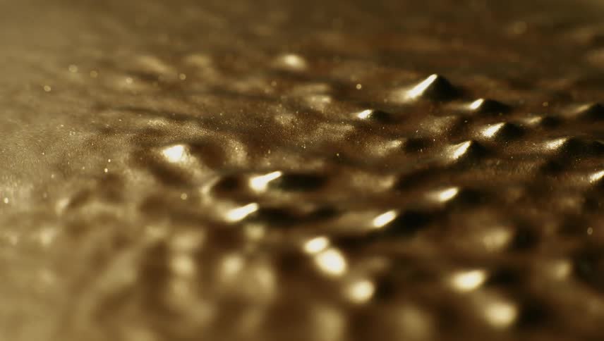 Spikes grow from a gold liquid substance and melt back down