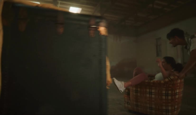 A man and woman laugh as the man pushes the woman around a room in a chair