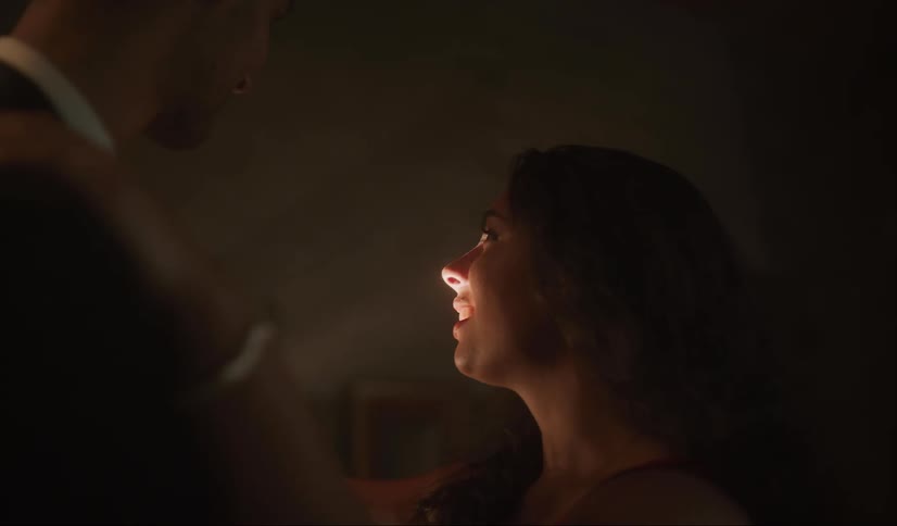 A woman smiles as she slow dances with a young man lights shining and glowing around them