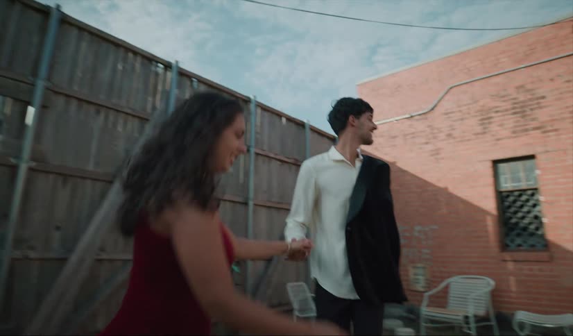 A man leads a woman in to a yard and then takes her hand and takes her to a building that they enter