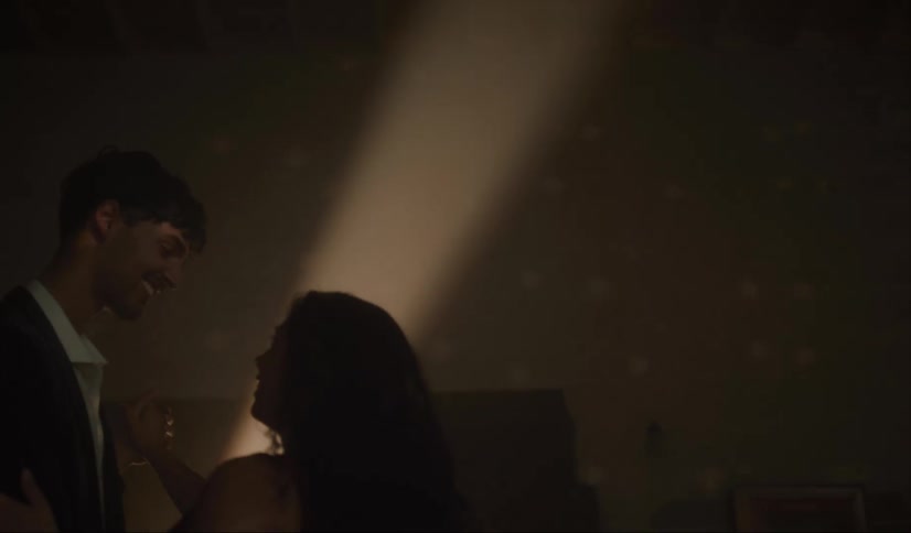 A man and woman dance indoors together and smile at one another