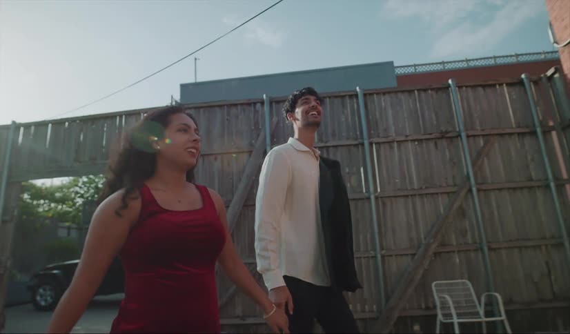 A man and woman walk through a gate and he grabs her hand and they go in to a building