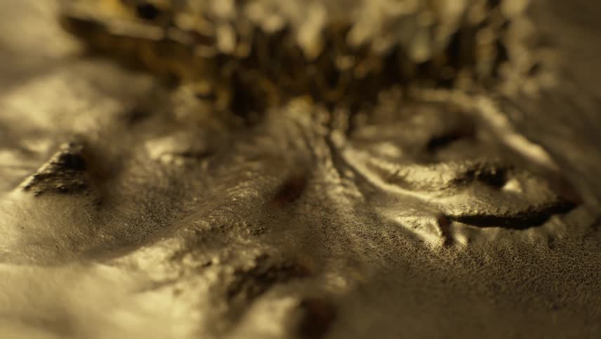 A gold substance flows around lumps as ripples melt and spikes emerge and melt back down