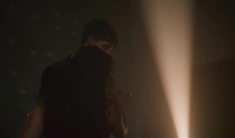 Couple slow dances in dim room lit by single spotlight and light reflected from a mirror ball