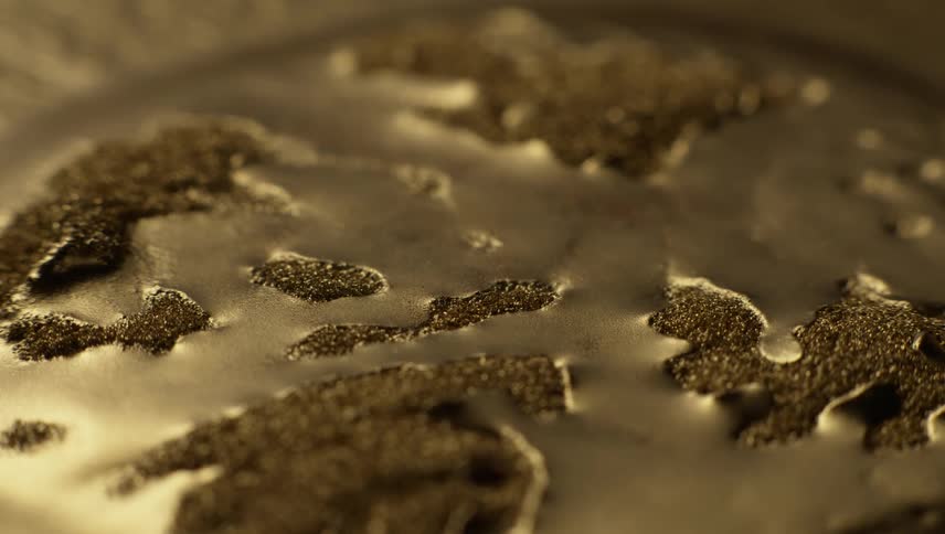 A puddle of gold liquid spikes dissipates into a smooth puddle surrounded by piles of glitter