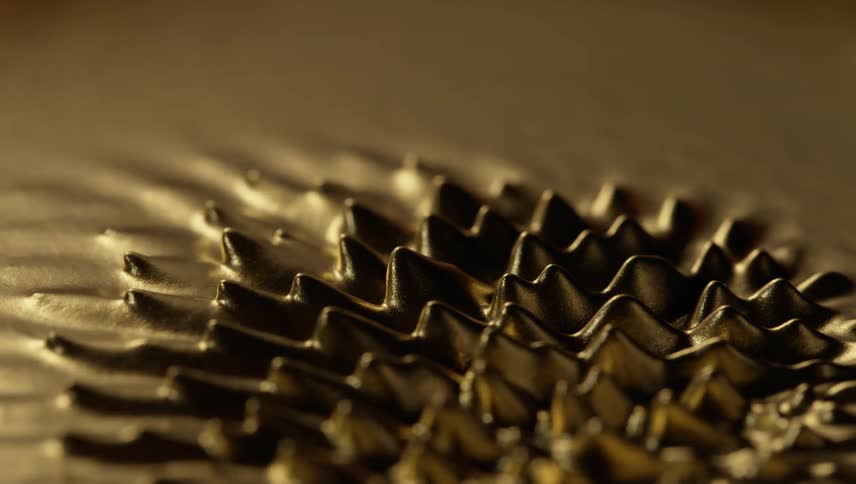 Small peaks emerge from metallic surface forming a circular shape before merging back into fluid