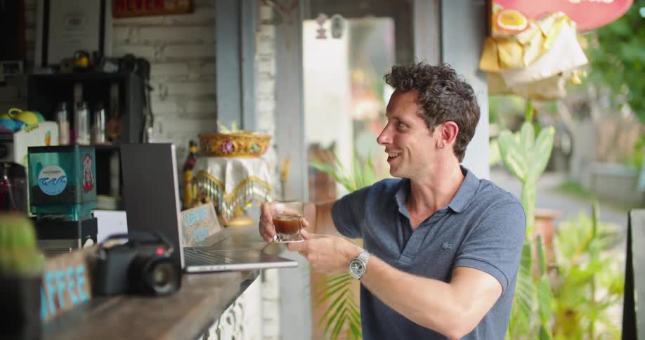 A man working at a bar smiles as he hands a man a drink