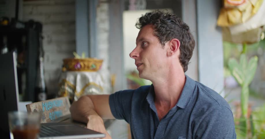 A man sitting at the counter of an outdoor cafe is moving his hands as he talks to the man behind the counter