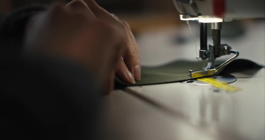 Hands and fingers feed fabric through a sewing machine to stitch