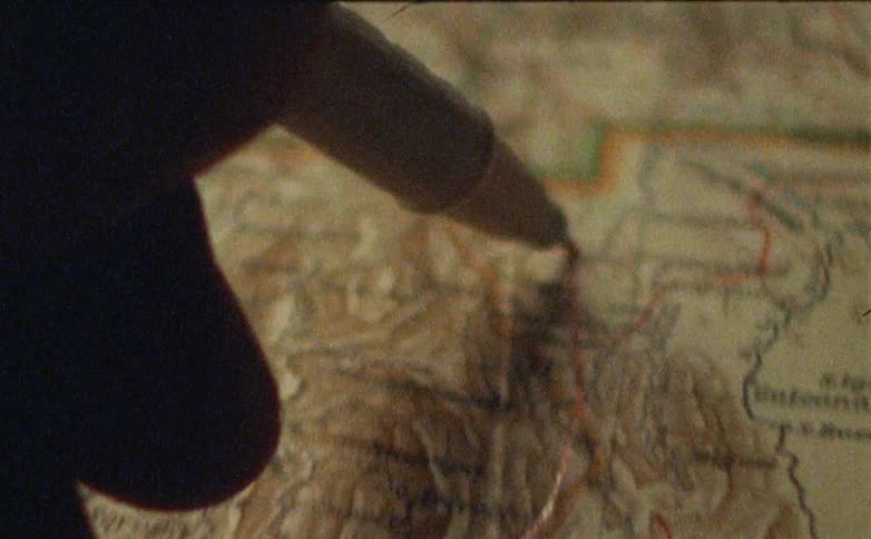 A hand holding a pen draws a red line on a map