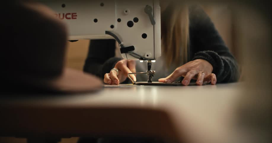 Blonde woman wearing black jacket uses sewing machine