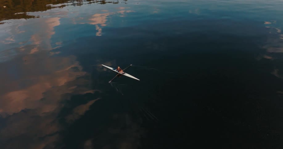 A person is sitting a canoe as it floats on the water as the sky and clouds reflect on the water