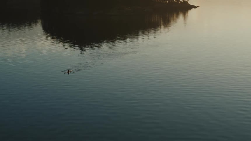 Person paddles kayak across water toward fog tinted red by sun