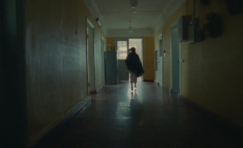 A girl runs down a hall in a house with a towel blowing behind her