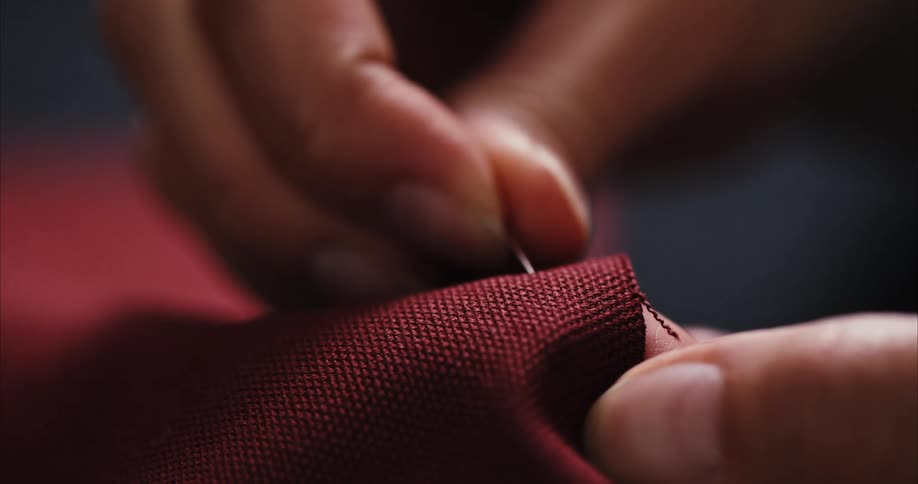 A woman pushes a pin through two pieces of fabric to hold them together for stitching