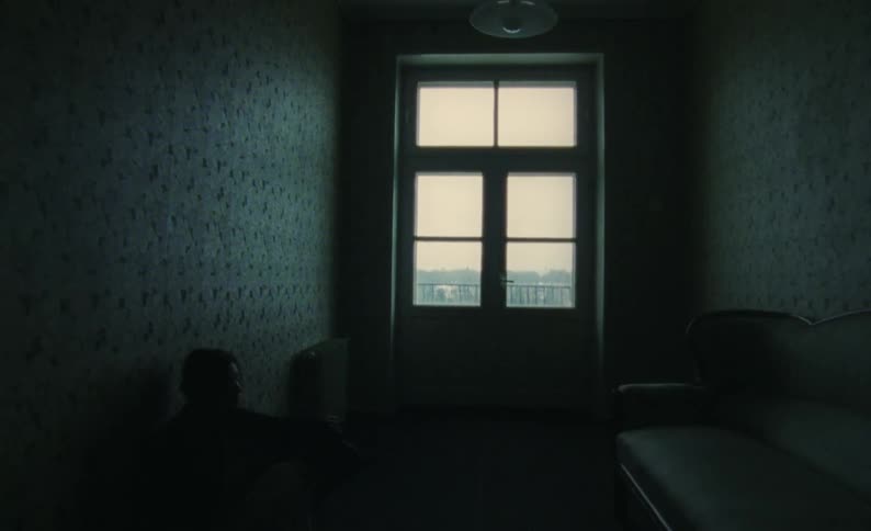 A woman walks down the dark hallway and sits on the floor