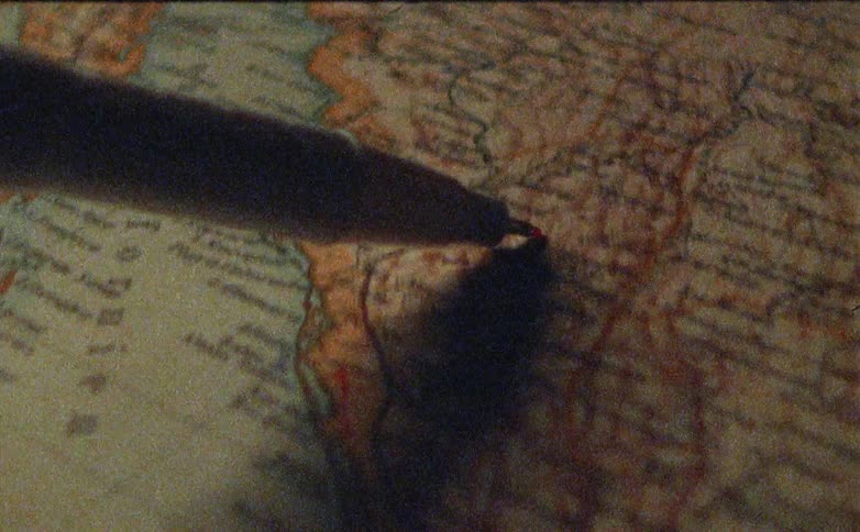 A person is tracing a pen on a map of the world