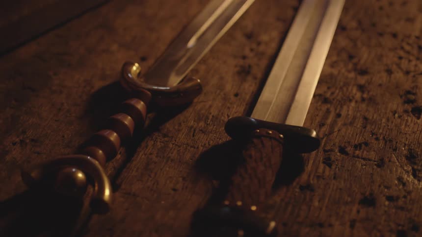 Two swords sit on a wooden table