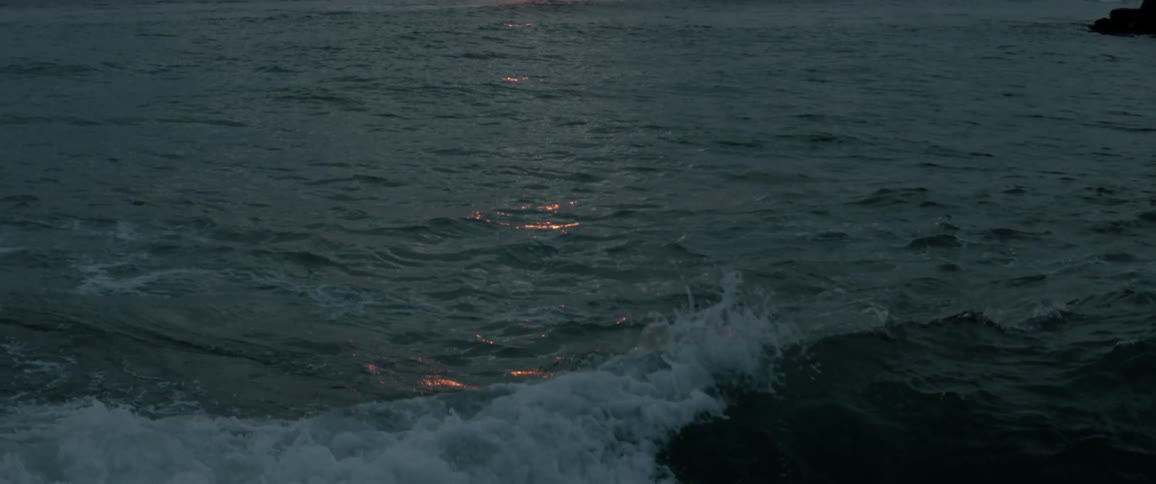 Waves splash and foam as they roll into shore and reflect light from the setting sun
