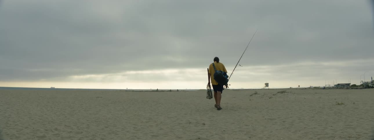 A man is walking on the beach with his fishing pole