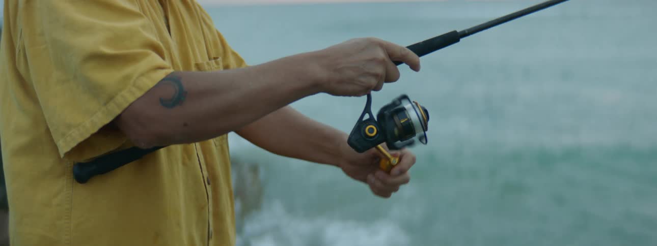 Man with ponytail and yellow shirt fishes with fishing rod on the coast