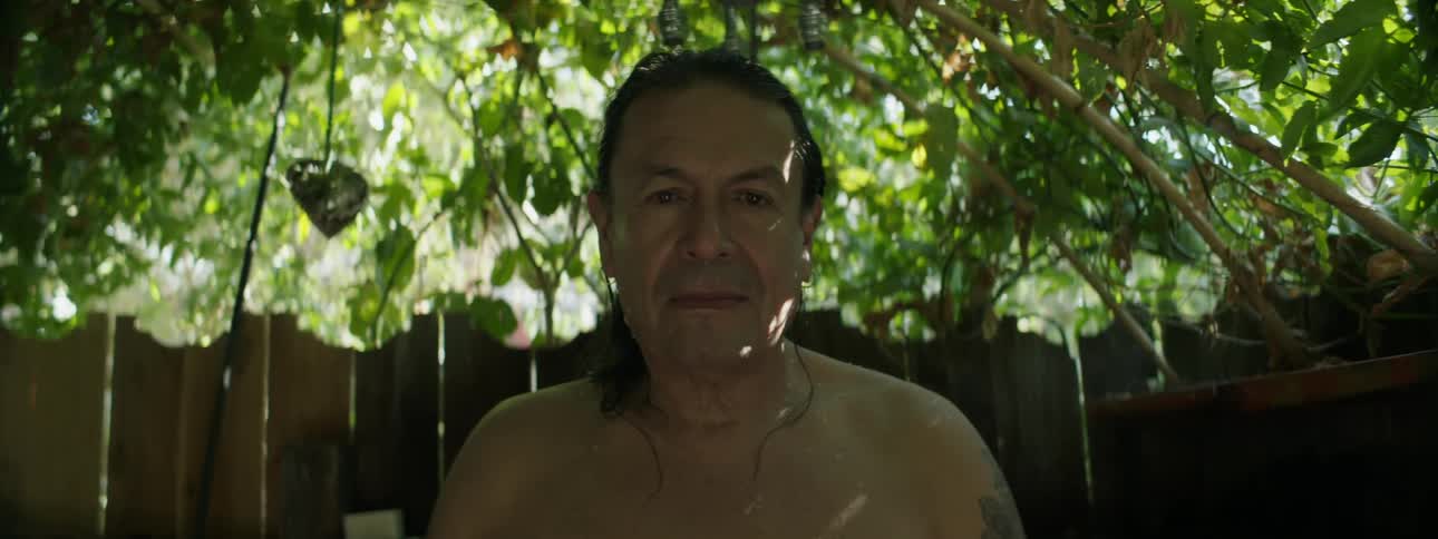 A man is standing near a wooden fence and trees with his eyes closed and then he opens them