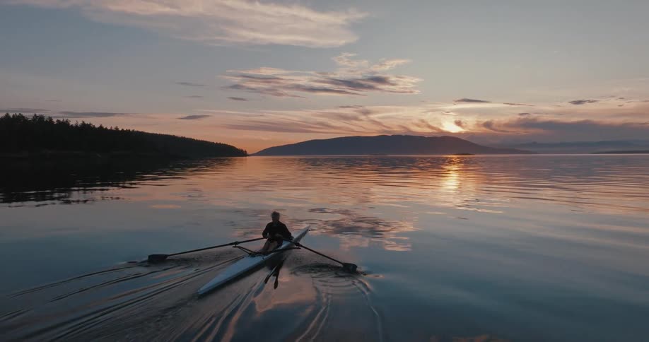 Silhouette of a man rowing a canoe as the sun is setting and the reflection is on the water