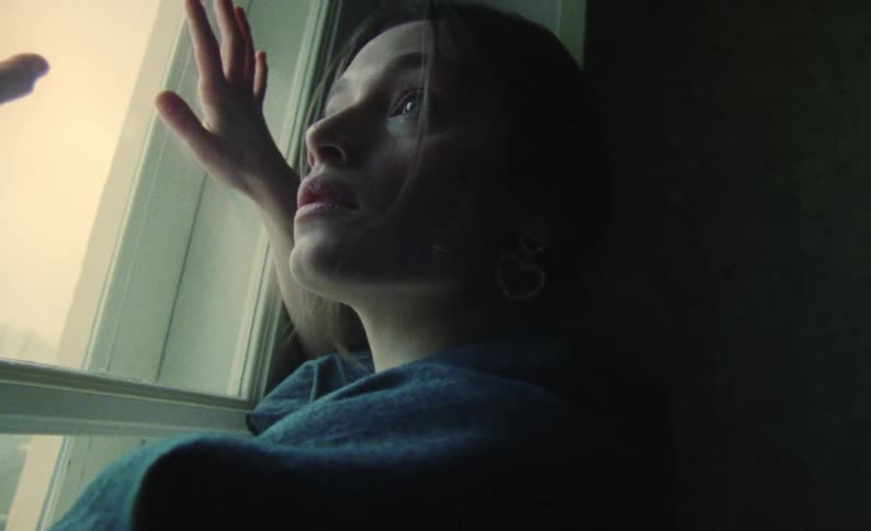 Woman examines glass of window showing view of town on hill
