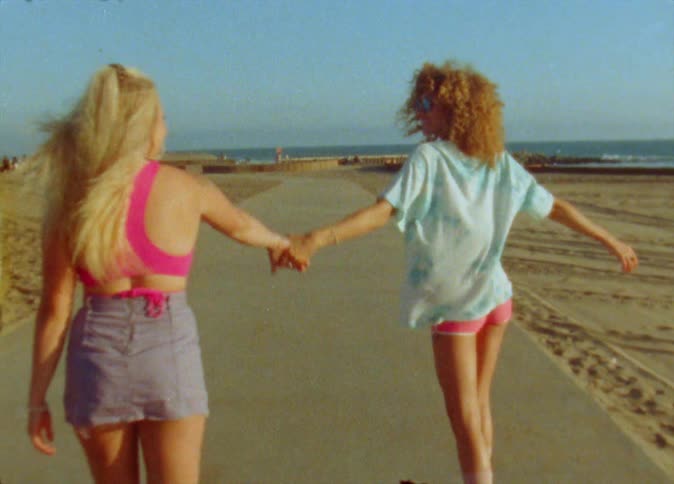 Two women hold hands while skating on the beach