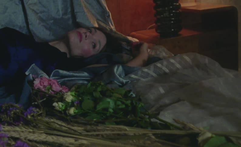 Woman lies on her back on bed near a bouquet of pink and white flowers