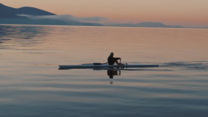 A man rows a canoe across a lake on a foggy evening