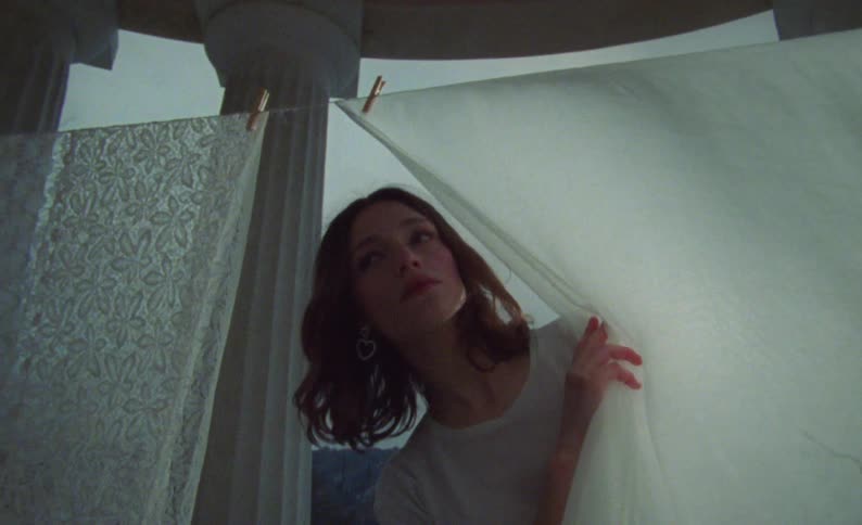 Woman hanging clothes on clothesline on porch peers around searchingly before continuing
