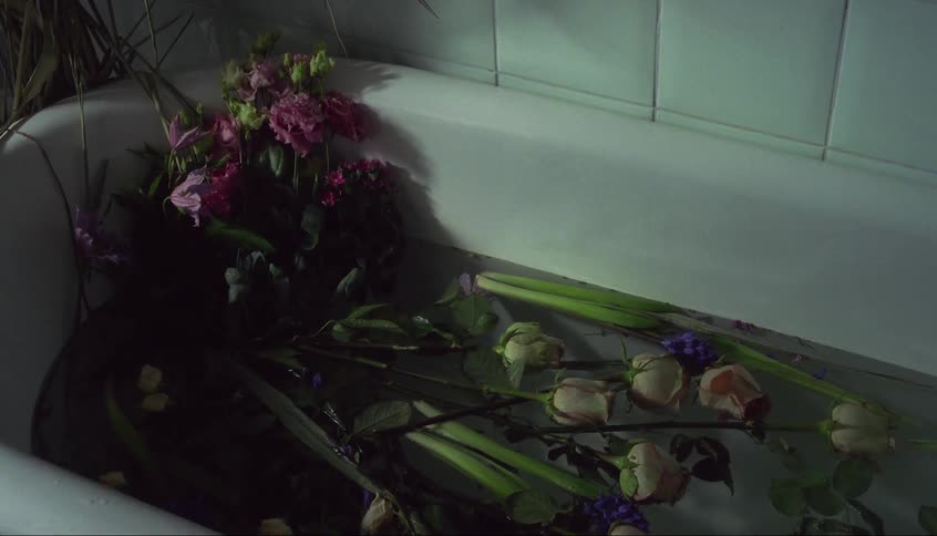A bouquet of flowers is in a bathtub filled with water and individual roses are floating away from the bouquet